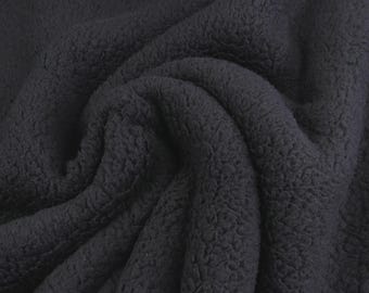 May include: A solid black fabric with a dense, curly, and textured pile surface. The material is arranged in soft, flowing folds that create deep shadows and highlights, emphasizing the thick, fuzzy, and uniform appearance of the textile.