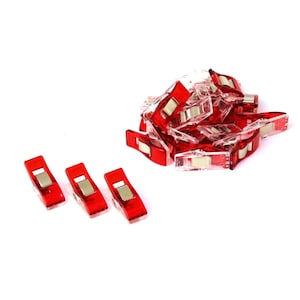 Pode incluir: Um monte de clipes de plástico vermelho com fechos de mola de metal. Existem quatro clipes em uma fila, separados do monte.