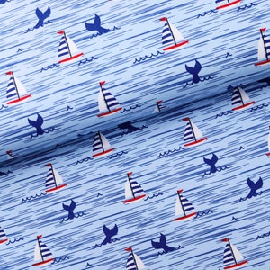 Peut inclure: Tissu bleu avec un motif répété de voiliers blancs et de queues de baleines bleues. Le fond est bleu clair avec de fines lignes blanches.