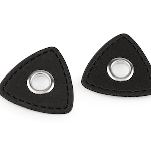 Könnte beinhalten: Zwei schwarze Leder-Plektronen mit einem silbernen Metallösen in der Mitte jedes Plektrons.