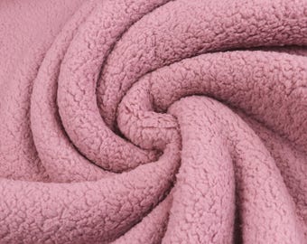 May include: A dusty rose colored fabric with a thick, textured, curly fleece pile. The material is arranged in a swirling, circular pattern that creates deep folds and shadows, highlighting the dense, soft, and fuzzy surface of the textile.