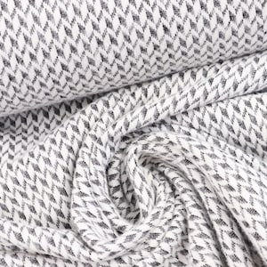 Puede incluir: Tela blanca con un patrón geométrico blanco y negro. La tela es tejida y tiene una superficie texturizada.