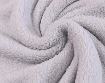 May include: A light gray fabric with a thick, plush, and fuzzy texture. The material is arranged in soft, swirling folds that create deep shadows and highlights, emphasizing the dense, curly pile of the fleece-like textile surface.