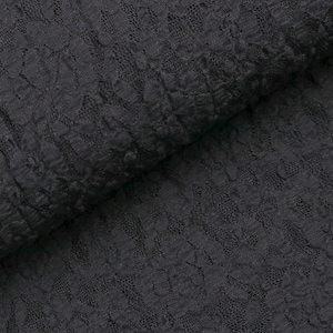 May include: Close-up of a dark gray lace fabric. The fabric has a floral pattern and a textured surface. The lace is folded, showing the intricate design and depth of the material. This fabric is suitable for apparel and craft projects.