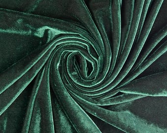 May include: A deep forest green velvet fabric featuring a dense, soft pile with a distinct sheen. The material is arranged in a swirling, circular pattern that creates natural folds, shadows, and highlights across the textured surface.