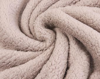 May include: A light beige fabric with a thick, plush, and curly sherpa texture. The material is arranged in deep, swirling folds that create a series of shadows and highlights, emphasizing the dense, soft, and fuzzy surface of the textile.