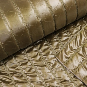 Può includere: Primo piano di tessuto trapuntato verde oliva. Il tessuto ha una texture lucida, leggermente stropicciata, con linee verticali cucite. Il tessuto è piegato, rivelando il lato inferiore di un colore più chiaro.