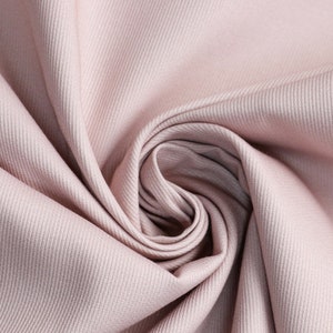 Könnte beinhalten: Nahaufnahme eines weichen, hellrosa Stoffes mit einer dezenten Rippenstruktur. Der Stoff ist drapiert und gefaltet, wodurch ein wirbelndes Muster entsteht. Die Farbe ist ein gedämpftes, staubiges Rosa, geeignet für Kleidung oder Heimdekoration.