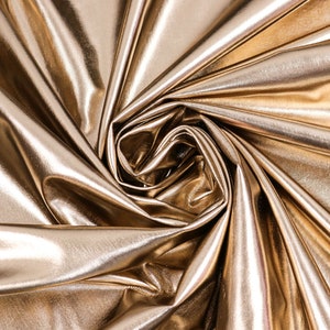 Könnte beinhalten: Nahaufnahme eines goldenen Metallic-Stoffes mit einer glatten, glänzenden Oberfläche. Der Stoff ist drapiert und gefaltet und erzeugt ein wirbelndes Muster.