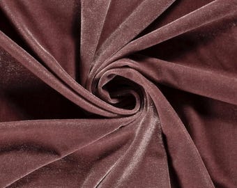 May include: A dusty rose velvet fabric featuring a dense, soft pile with a subtle sheen. The material is gathered into a central swirl, creating deep, flowing folds and shadows that highlight the rich, muted pinkish-brown color of the textile.