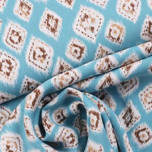 Op de afbeelding: Blauwe stof met een wit en bruin geometrisch patroon. De stof is gevouwen en heeft een zachte, vloeiende textuur.