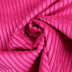 Könnte beinhalten: Nahaufnahme eines leuchtend pinkfarbenen Cordstoffs. Der Stoff ist gefaltet und drapiert und zeigt die gerippte Textur und das weiche, plüschige Gefühl. Die Farbe ist ein helles, sattes Pink mit sichtbaren vertikalen Rippen.