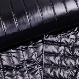 May include: Close-up of a shiny, black quilted fabric. The fabric is folded over, revealing both the vertical and diamond-stitched patterns. The material has a glossy, reflective surface.