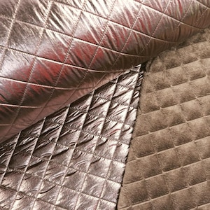 May include: Two pieces of quilted fabric, one in a metallic rose gold color and the other in a brown color. Both fabrics have a diamond-shaped quilting pattern.