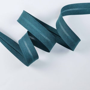 Könnte beinhalten: Tealblaues Stoffband mit einem dezenten Glanz und zwei weißen Streifen, die in der Mitte verlaufen. Das Band ist gefaltet und zu einer Spirale gedreht.