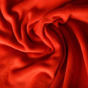 Puede incluir: Primer plano de una vibrante tela polar roja lisa. El material es suave y afelpado, con pliegues y texturas visibles que crean sombras y luces. La tela parece cálida y acogedora, adecuada para mantas o prendas de vestir.