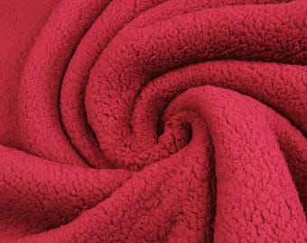 May include: A deep red fabric with a thick, textured, and fuzzy fleece surface. The material is arranged in a swirling, circular pattern that creates deep folds and shadows, highlighting the dense, soft, and plush pile of the textile.