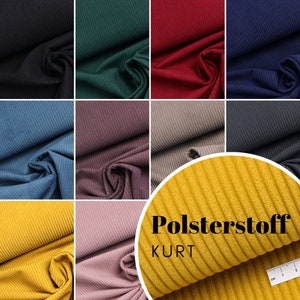 Könnte beinhalten: Eine Auswahl von 10 verschiedenen Farben Cordstoff. Der Stoff ist gerippt und hat eine weiche Textur. Der Stoff ist mit "Polsterstoff KURT" gekennzeichnet.