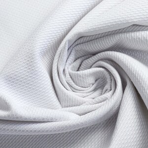 Peut inclure: Gros plan sur un tissu blanc avec un motif texturé en nid d'abeille. Le tissu est étroitement enroulé, créant un effet de spirale. La matière semble douce et souple, avec de subtiles variations de lumière et d'ombre.