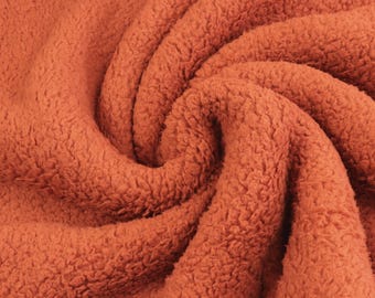 May include: A thick, textured fabric in a solid burnt orange color. The material features a dense, curly, fleece-like pile that creates deep, swirling folds and shadows across the surface, highlighting the soft and fuzzy nature of the textile.