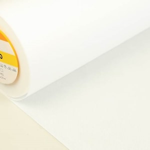 Op de afbeelding: Een witte rol stof met een geel label met de tekst "Vlieseline S 320 100% PES 90cm x 25m".