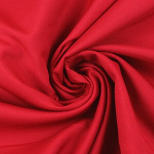 Pode incluir: Close-up de um tecido vermelho vibrante, disposto em espiral. O material parece liso e apresenta dobras e sombras que criam profundidade. A cor rica do tecido sugere um possível uso para roupas ou decoração.