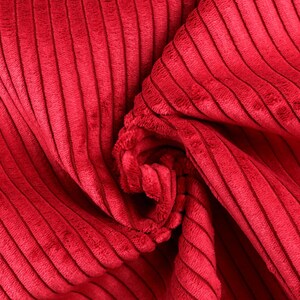 Könnte beinhalten: Nahaufnahme eines roten Cordstoffs mit weicher, plüschiger Textur. Der Stoff ist gefaltet und zerknittert und zeigt die vertikalen Rippen des Cordstoffs.