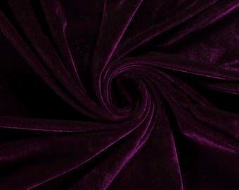 May include: A deep purple velvet fabric featuring a dense, soft pile texture. The material is arranged in a central spiral swirl, creating natural folds and highlights that emphasize the rich, dark violet color and the reflective sheen of the fabric.