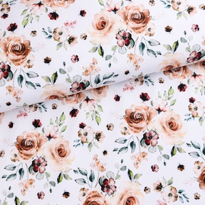 Op de afbeelding: Witte stof met een bloemenpatroon. Het ontwerp toont grote, open rozen in bruine en perziktinten, afgewisseld met kleinere bloemen en groene bladeren. De stof is waarschijnlijk katoen of een vergelijkbaar materiaal.