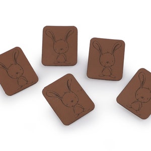 May include: Five brown leather patches with a black outline of a bunny rabbit on each.