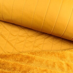 Puede incluir: Primer plano de una tela acolchada de color amarillo mostaza con una textura suave y peluda en la parte inferior.