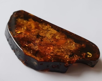 May include: A large, irregular piece of amber with a dark brown border and a translucent, golden interior. The amber has a cloudy, cloudy appearance with small, white inclusions.