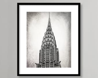 Puede incluir: Una fotografía en blanco y negro del edificio Chrysler en la ciudad de Nueva York. El edificio es alto y delgado, con una aguja puntiaguda en la parte superior. La fotografía tiene un aspecto vintage y texturado.