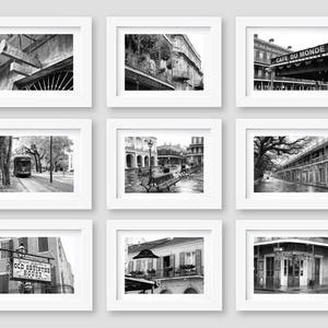 May include: Nine black and white photographs of New Orleans, Louisiana, framed in white frames. The photos show various scenes of the city, including streetcars, buildings, and street signs. The photos are arranged in a 3x3 grid.