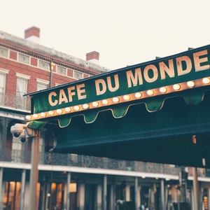 May include: A green awning with white lights and the text "Cafe Du Monde" in white letters. The awning is over a brick building with windows.