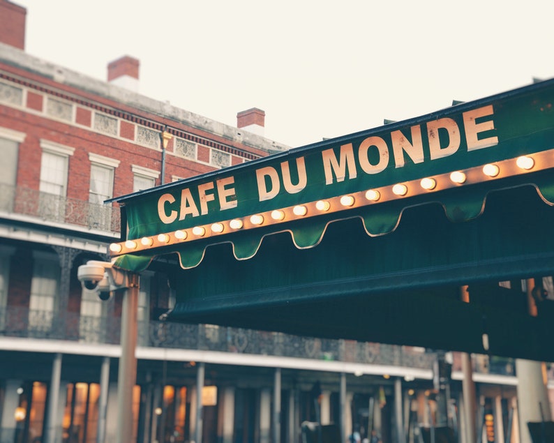 May include: A green awning with white lights and the text "Cafe Du Monde" in white letters. The awning is over a brick building with windows.