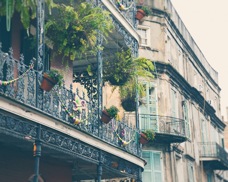 Pu&ograve; includere: Un edificio d'epoca con un balcone in ferro battuto decorato con perline viola, verdi e dorate. Il balcone ha diverse piante e fiori in vaso. L'edificio &egrave; dipinto in tonalit&agrave; di grigio e bianco.