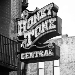 May include: Black and white photograph of a neon sign that reads "Honky Tonk Central" in a retro font. The sign is mounted on a brick building.