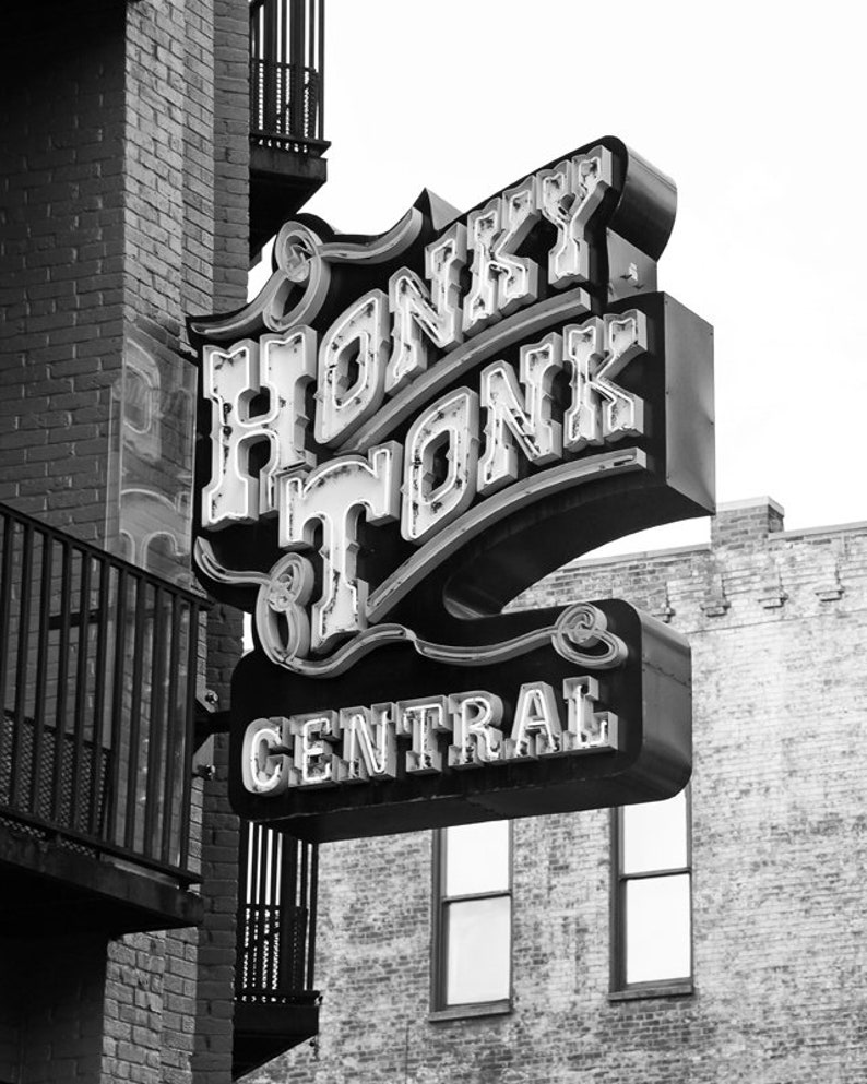 May include: Black and white photograph of a neon sign that reads "Honky Tonk Central" in a retro font. The sign is mounted on a brick building.