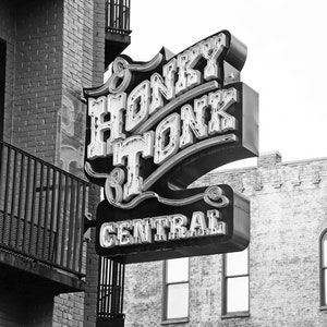 May include: Black and white photograph of a neon sign that reads "Honky Tonk Central" in a retro font. The sign is mounted on a brick building.