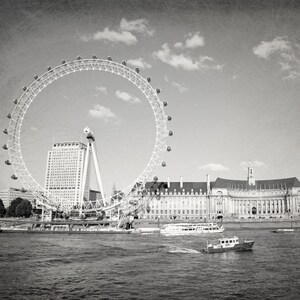 Op de afbeelding: Een zwart-witfoto van het reuzenrad London Eye, een groot gebouw en een rivier met boten. Het reuzenrad staat op de voorgrond en het gebouw op de achtergrond.