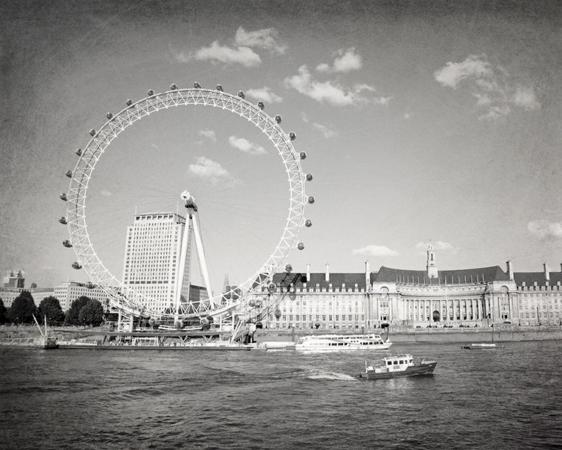 Op de afbeelding: Een zwart-witfoto van het reuzenrad London Eye, een groot gebouw en een rivier met boten. Het reuzenrad staat op de voorgrond en het gebouw op de achtergrond.
