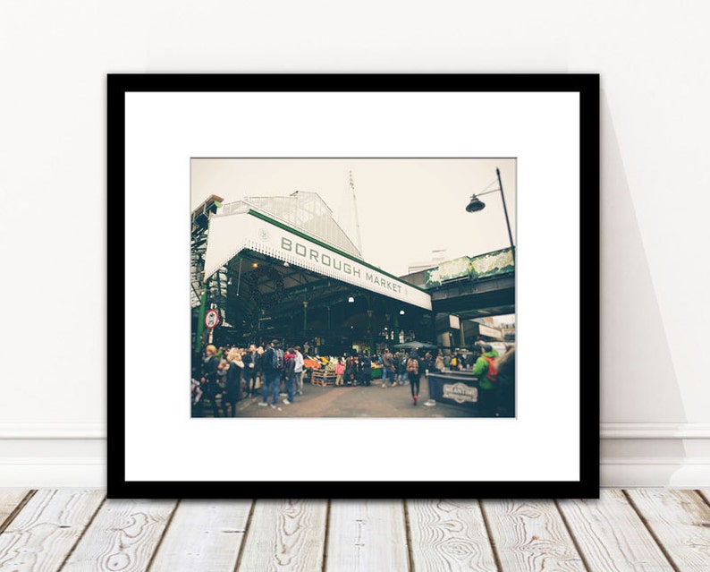 May include: Framed print of Borough Market, London. The image shows the market entrance with the words "BOROUGH MARKET" on a white awning. People are seen in the market, with a vintage aesthetic.