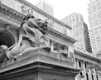 May include: A black and white photo of a large stone lion statue in front of a building. The lion is sitting on a pedestal and has its head turned to the right. The building behind the lion has columns and a large inscription that reads "LIBRARY AND MUSEUM".