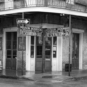 Pu&ograve; includere: Una fotografia in bianco e nero di un edificio in mattoni con un cartello che recita "Maison Bourbon Dedicato alla preservazione del jazz". In primo piano c'&egrave; un idrante.