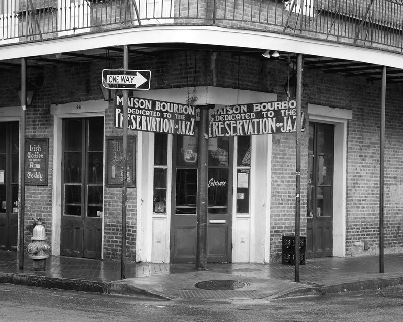 Pu&ograve; includere: Una fotografia in bianco e nero di un edificio in mattoni con un cartello che recita "Maison Bourbon Dedicato alla preservazione del jazz". In primo piano c'&egrave; un idrante.