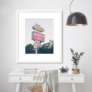 May include: A framed photograph of a vintage motel sign with the words "Madonna Inn" in pink and blue lettering. The sign is on a white pole with a red and white striped awning. The sign is set against a backdrop of trees and a cloudy sky.