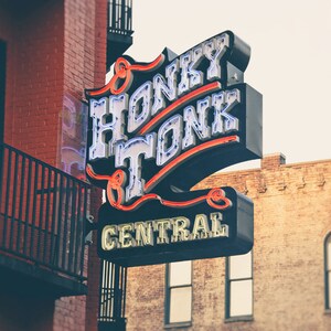 May include: A neon sign with the words "Honky Tonk Central" in white letters with red outlines. The sign is mounted on a brick building.