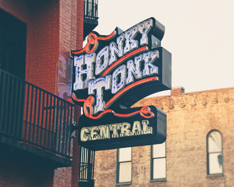 May include: A neon sign with the words "Honky Tonk Central" in white letters with red outlines. The sign is mounted on a brick building.