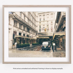 May include: A black taxi cab is parked in front of a grand building with the word "SAVOY" above the entrance. The building has a classic architecture with tall windows and ornate details. The scene is captured in a vintage style with a soft, faded color palette.